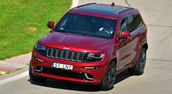 Czerwony Jeep Grand Cherokee z indywidualnymi tablicami rejestracyjnymi "S1 LNY" na torze wyścigowym.