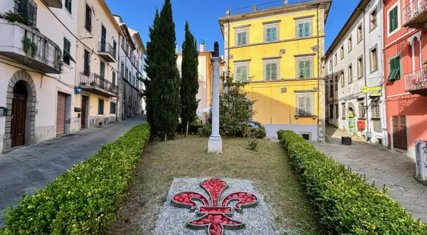 Fivizzano cosa vedere: un'aiuola con un giglio rosso e un monumento in un vicolo con case colorate.