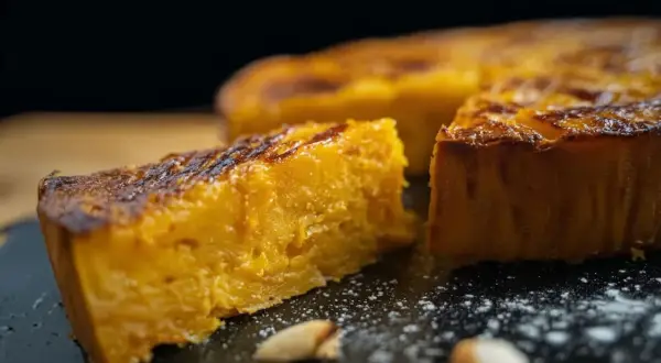 Un morceau de gâteau patate douce, doré et moelleux, est présenté sur une assiette noire saupoudrée de sucre glace.