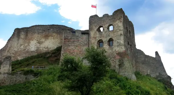 Zamek Czorsztyn, majestatyczne ruiny na wzgórzu, dumnie prezentuje polską flagę na tle błękitnego nieba.