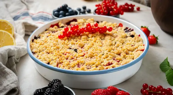 Ein köstlicher Beeren Crumble mit roten Johannisbeeren, Blaubeeren und Himbeeren, garniert mit frischen Beeren und Zitronenspalten.