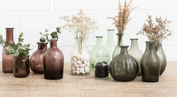Variedad de jarrones de cristal grandes, algunos con ramas secas y hojas verdes, perfectos para decorar.