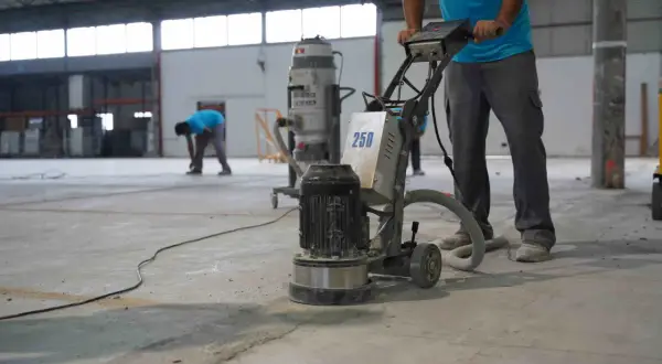 Trabajadores pulen un suelo de hormigón con una máquina. Se muestra cómo hacer hormigón para suelo, preparando la superficie.