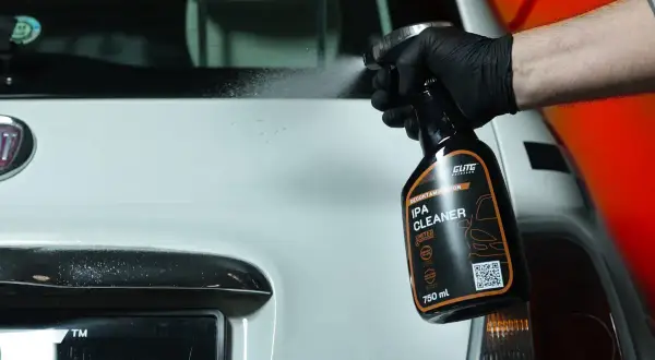 Ręka w czarnej rękawiczce rozpyla środek IPA CLEANER na biały samochód. Idealny do dekontaminacji lakieru.