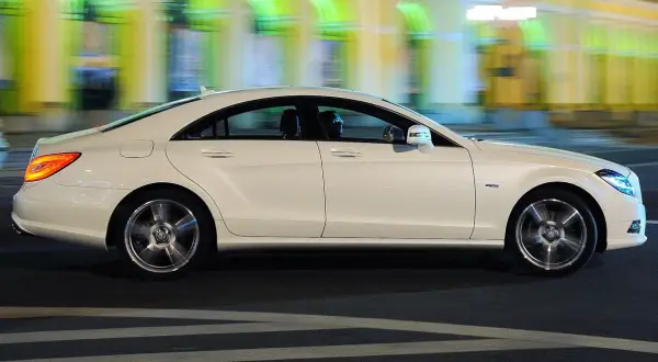 Biały Mercedes CLS 63 AMG mija nocą rozmyte światła miasta, jego sylwetka jest dynamiczna i elegancka.