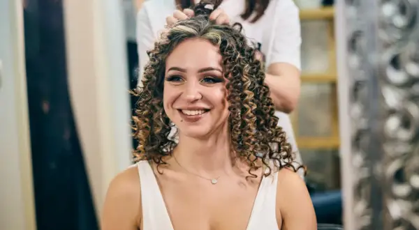Une femme souriante se fait faire une permanente chez le coiffeur. Ses cheveux bouclés sont magnifiques.