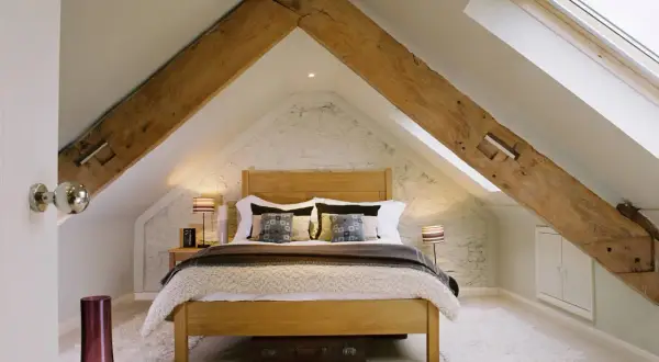 Dormitorio acogedor bajo un tejado con vigas de madera expuestas, ideal para levantar tejado para hacer buhardilla.