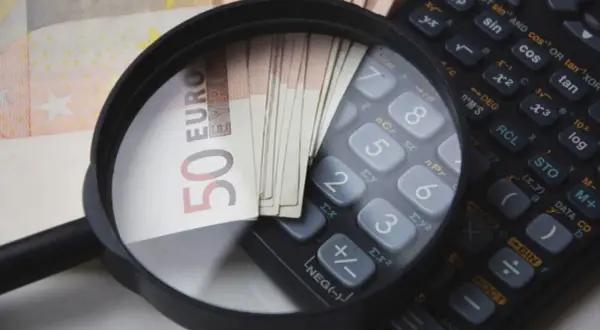 Lupe über 50-Euro-Scheinen und einem Taschenrechner. So wird die Frage "wie viel verdient man im Referendariat" visuell beleuchtet.