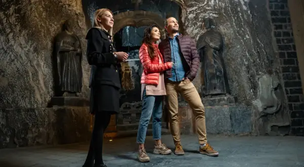Przewodniczka oprowadza parę po kopalni soli w Wieliczce. Trasa turystyczna zachwyca rzeźbami i surowym pięknem.