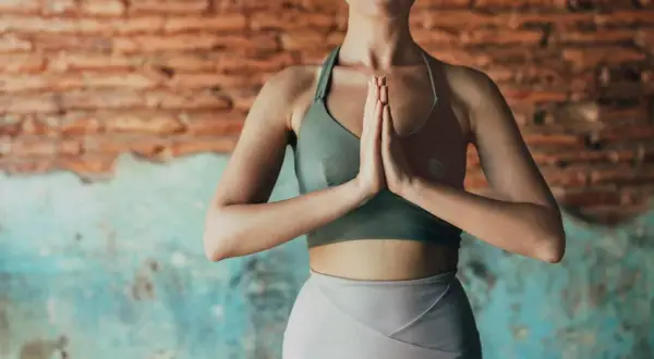 Mujer en postura de oración, practicando tantra yoga. Fondo de ladrillo y pared desgastada.