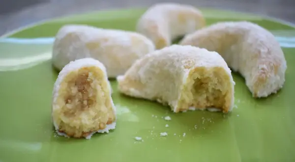 Petits gâteaux en forme de croissant, saupoudrés de sucre glace. Ces délices ressemblent à des cornes de gazelle, prêts à être dégustés.