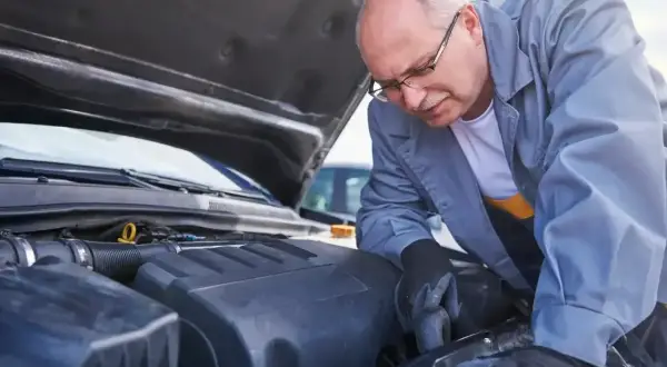 Mechanik w okularach pochyla się nad silnikiem, przygotowując się do wymiany chłodnicy.