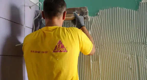 Operaio con maglia gialla Sika applica colla per incollare piastrelle su piastrelle parete.