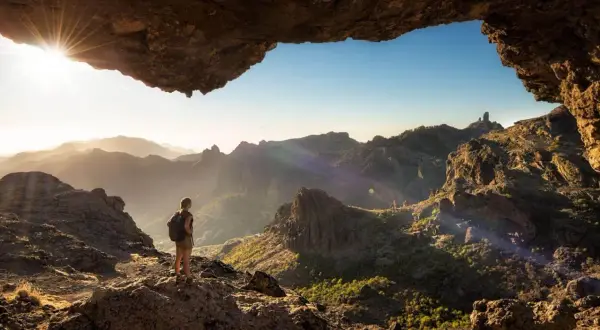 Una persona con mochila admira el paisaje montañoso al amanecer, disfrutando de unas increíbles caminatas Gran Canaria.