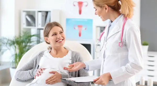 Lekarka rozmawia z ciężarną pacjentką o niedoczynności tarczycy w ciąży. Uśmiechnięta przyszła mama słucha z uwagą.