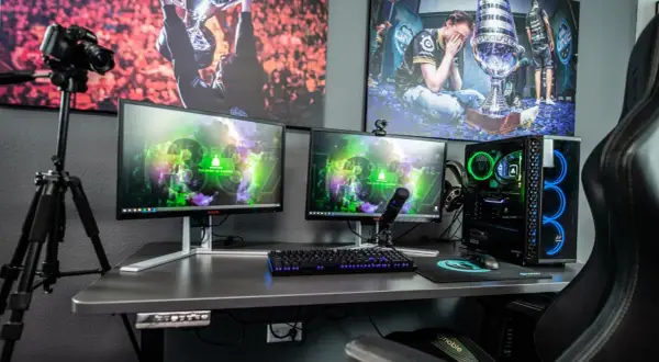 Ein Streamer-Setup: Zwei Monitore, Mikrofon, Kamera auf Stativ, Gaming-PC mit blauer Beleuchtung und Bilder von E-Sport-Erfolgen. So macht ein Streamer seine Inhalte.