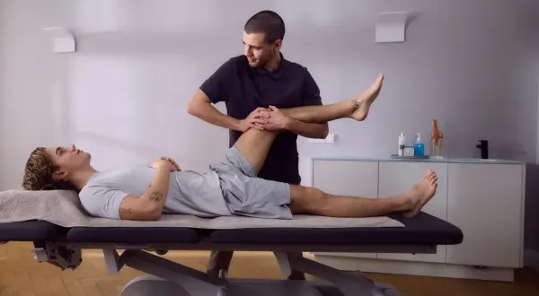 Physiotherapeut führt krankengymnastik hws durch, indem er das Bein eines liegenden Patienten sanft bewegt.