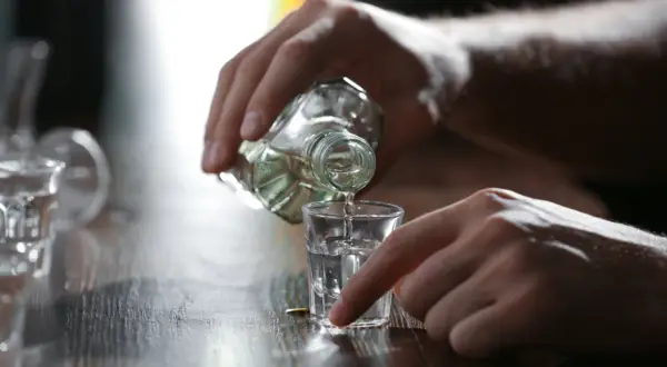 Dłoń nalewa alkohol do kieliszka. Może to być pierwszy kieliszek wypity na czczo.