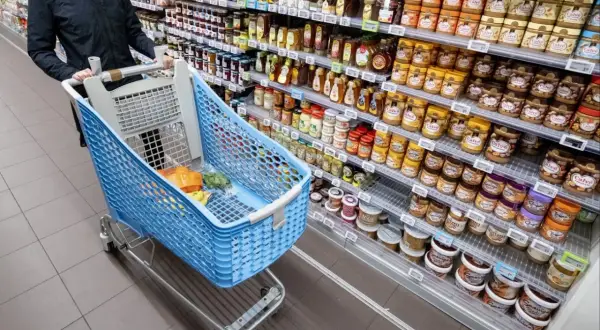 Kosz z zakupami w holenderskim supermarkecie. Na półkach dżemy, miody i masła orzechowe. Sprawdzam ceny w Holandii.