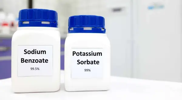 Zwei weiße Behälter mit blauen Deckeln stehen nebeneinander. Auf dem linken Behälter steht "Sodium Benzoate 99.5%", auf dem rechten "Potassium Sorbate 99%".