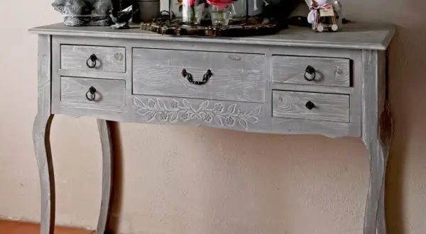 Console grise patinée, ornée de motifs floraux sculptés. Ce meuble à tiroirs, idéal pour un intérieur cosy, invite à y poser des objets décoratifs.
