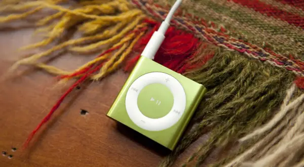 A green iPod Shuffle, a relic from when MP3 players were invented, rests on a wooden surface next to a colorful, fringed scarf.