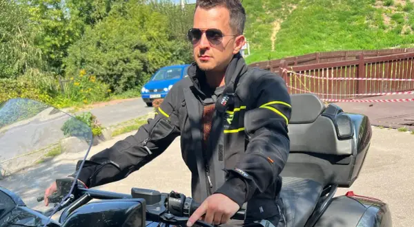 Mężczyzna w okularach przeciwsłonecznych i czarnej kurtce motocyklowej, gotowy na podróż.