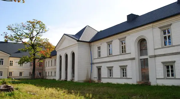Pałac w Siemianowicach Śląskich, biała fasada z arkadowymi oknami i ciemnym dachem, otoczony zielenią i jesiennym drzewem.