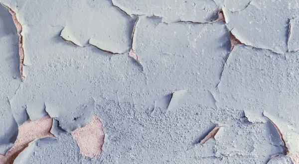 Texture d'un plafond avec peinture écaillée, révélant la couche inférieure rosée. Les craquelures créent un motif abstrait.