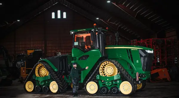 Man bredvid en stor grön John Deere-traktor i en lada. Frågan "hur länge håller diesel" kan vara relevant för denna maskin.
