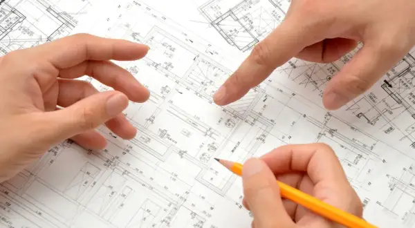 Dłonie analizują plany architektoniczne, wskazując na szczegóły dotyczące metrażu mieszkania i rozmieszczenia pomieszczeń.