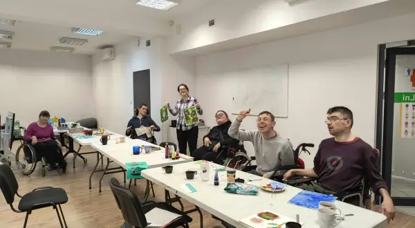 Grupa osób z niepełnosprawnościami uczestniczy w zajęciach plastycznych w ośrodku pomocy społecznej dzielnicy Bielany m. st. Warszawy.