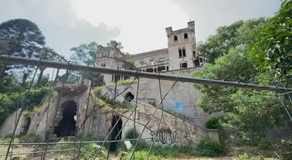 Ruines d'un château délabré, envahi par la végétation et couvert de graffitis. Un portail orné et des tours menacent de s'effondrer. Une scène d'urbex flippant.