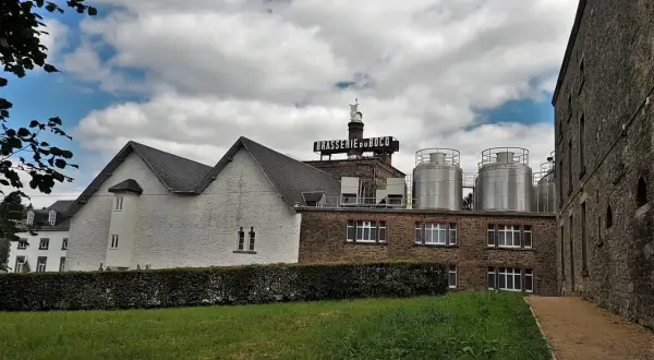 Edificio della Brasserie du Bocq con serbatoi in acciaio inox e un cielo nuvoloso.