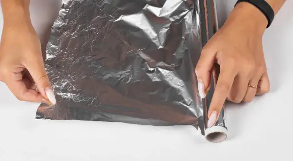 Dłonie rozwijają folię aluminiową, by zapobiec powstawaniu kożucha na sosie. Jak go zabezpieczyć folią?