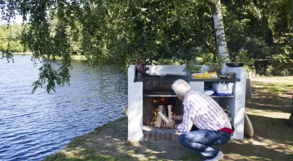 Man tänder en brasa vid en murad grillplats vid en sjö.