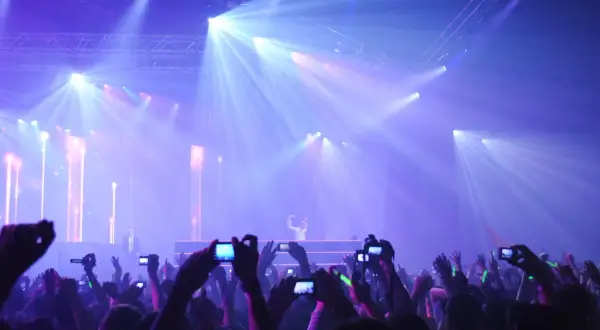 Tłumy na rave festivalu filmują DJ-a na scenie oświetlonej laserami.