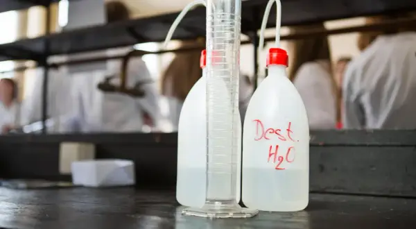 Bouteilles d'eau distillée et éprouvette graduée sur un établi de laboratoire, prêtes pour la stérilisation eau chaude.