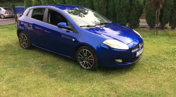 Błękitny Fiat Bravo 1.4 T-Jet zaparkowany na trawniku, za nim żywopłot.