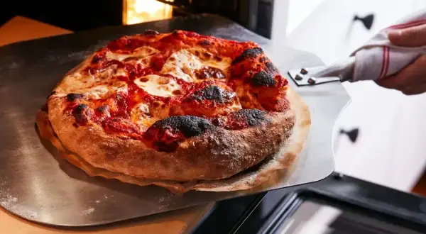 Gorąca, świeżo upieczona pizza z serem i sosem pomidorowym jest wyjmowana z pieca. Idealnie, ile piec pizze!