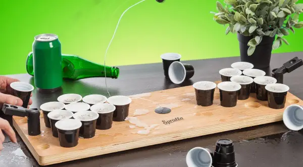 En rolig lekar fest vuxna inomhus med beer pong-spel. En boll flyger mot muggarna på träplattan.
