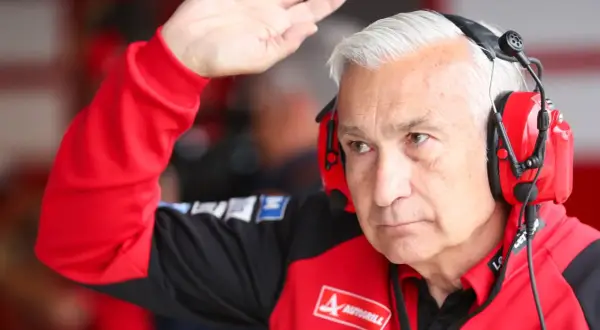 Davide Tardozzi, con auriculares rojos, saluda con la mano. Viste una chaqueta roja de equipo de carreras.