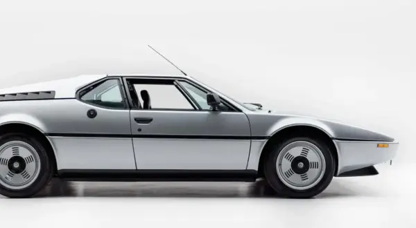 Srebrne BMW M1 E26 widziane z boku, z otwartymi drzwiami.
