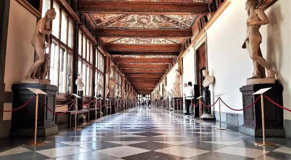 Corridoio della **Gallerie des Offices Florence**, con statue classiche, soffitto affrescato e pavimento a scacchi.