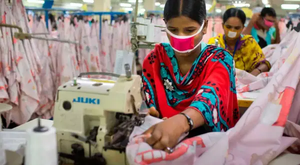 Frauen mit Masken arbeiten an Nähmaschinen. Sie sind Teil einer nachhaltigen Textilproduktion, die auf faire Arbeitsbedingungen und umweltfreundliche Prozesse setzt.