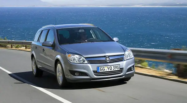 Srebrny Opel Astra H kombi jedzie drogą nad morzem.