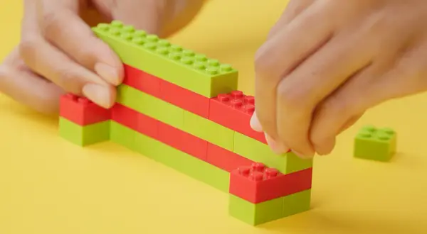 Dziecko buduje z zielonych i czerwonych klocków, pokazując, jak zbudować z klocków lego.