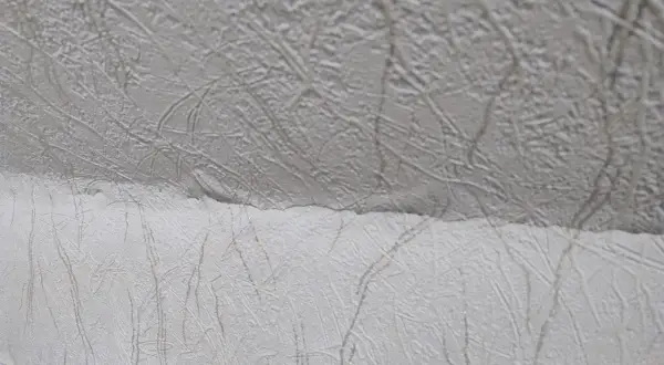 Detaljbild av vit, mönstrad tapet som täcker ett snedtak. Mönstret liknar kvistar eller ådring.