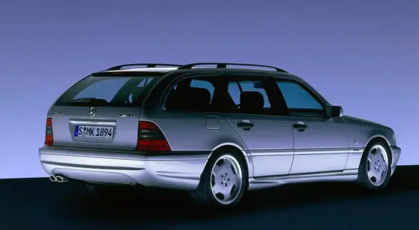 Srebrny Mercedes C klasa 2000 kombi z felgami AMG, widziany z tyłu, na tle niebieskiego gradientu.