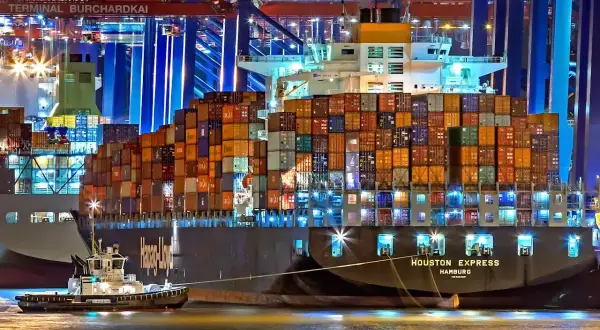 Kontenerowiec "Houston Express" z Hamburgu z ładunkiem kontenerów w porcie nocą, holowany przez statek.
